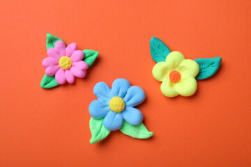 Wall Mural - Colorful flowers with leaves made from play dough on orange background, flat lay