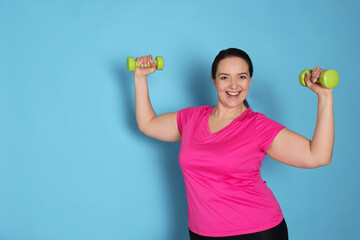 Sticker - Happy overweight woman doing exercise with dumbbells on light blue background, space for text