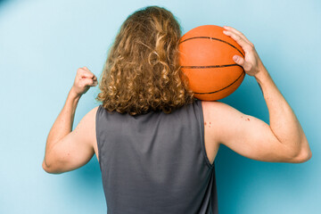 Wall Mural - Young caucasian man playing basketball isolated on blue background