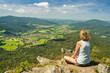 A woman sitting on mount Osser, overlooking the landscape of Lamer Winkel with the small town Lam in the Bavarian Forest