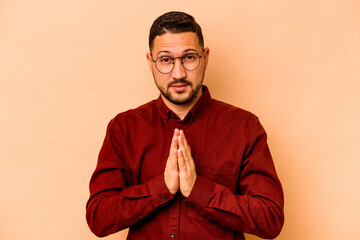 Young hispanic man isolated on beige background praying, showing devotion, religious person looking for divine inspiration.