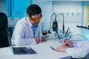  Portrait of a scientist working in the lab examines a test tube with liquid.