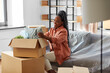 © Syda Productions - moving, people and real estate concept - happy smiling woman unpacking boxes sitting on sofa at new home