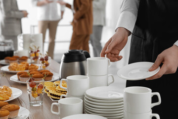 Canvas Print - Waitress near table with dishware and different delicious snacks during coffee break, closeup