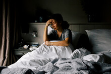 Mentally Depressed Woman Sitting With Head In Hand On Bed At Home
