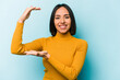 © Asier - Young hispanic woman isolated on blue background holding something little with forefingers, smiling and confident.