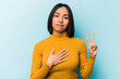 © Asier - Young hispanic woman isolated on blue background taking an oath, putting hand on chest.