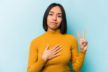 young hispanic woman isolated on blue background taking an oath, putting hand on chest.