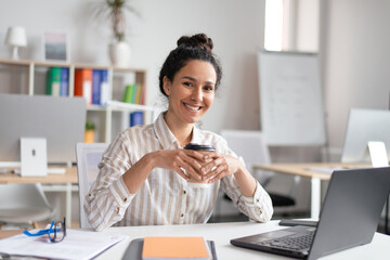 Sticker - Happy businesswoman working on laptop and drinking takeaway coffee while working in office, sitting at workplace