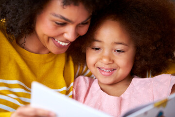 Mother And Daughter Relaxing On Sofa At Home Reading Book Together