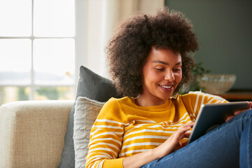 Woman Relaxing On Sofa At Home Using Digital Tablet To Stream Movie Or Shop Online