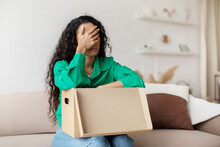 Unhappy Female Buyer Unpacking Cardboard Box After Shopping Failure Indoors