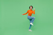 Full body young woman 20s wear orange turtleneck doing winner gesture celebrate clenching fists say yes raise up leg isolated on plain pastel light green color background. People lifestyle concept