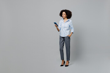 Wall Mural - Full body successful young employee business corporate lawyer woman of African American ethnicity in classic formal shirt work in office hold in hand use mobile cell phone isolated on grey background.