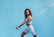 Strong and fit woman doing intense training with resistance band. Young female athlete exercising with stretching band on blue background.