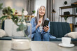 © sofiko14 - People, home and using gadgets. Pretty dreamy senior lady woman, sitting on the couch at cozy living room indoors and using smartphone for typing message or serfing social networks.