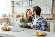 Happy young caucasian couple look at each other, drink tea, enjoy free time at weekend in modern kitchen