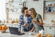 Leinwandbild Motiv Happy young european husband with stubble and wife shopping online and show credit card in modern kitchen
