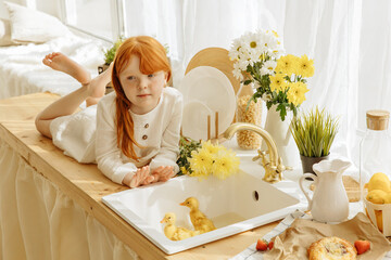 Wall Mural - Little girl and cute ducklings are sitting in a basket in the kitchen.