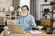 © sofiko14 - Smiling mature businessman using modern laptop for video chat at remote work. Handsome man with grey beard sitting at table with laptop, lamp and papers. Technology, remote work, freelance concept.