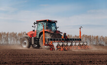Spring Sowing Season. Farmer With A Tractor Sows Corn Seeds On His Field. Planting Corn With Trailed Planter. Farming Seeding. The Concept Of Agriculture And Agricultural Machinery.