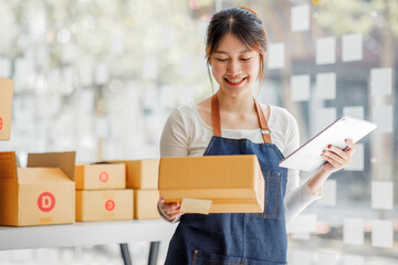 Startup happy Asian woman business owner works with a box at home, prepare parcel delivery SME supply chain, procurement, package box to deliver to customers, Online SME business entrepreneurs ideas,