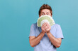 © khosrork - Portrait of handsome young adult bearded man peeping out euro banknotes with playful look, enjoying big jackpot, financial success. Indoor studio shot isolated on blue background.