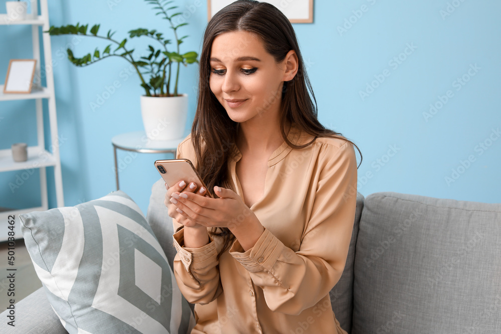 Beautiful young woman with mobile phone reading message at home