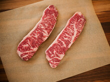 Two Raw Strip Steaks On Parchment Paper.