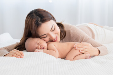 Beautiful asian mom supports and tenderly cuddles newborn baby gently while baby sleeping. Young woman kissing and touching on back child with love and tender. Mother and infant spend time together.