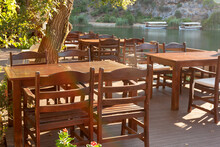 Wooden Empty Tables With Massive Chairs In Restaurant On River Bank.