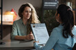 © AnnaStills - Rear view of businesswoman examining resume of young girl while she sitting at table and telling about herself at interview
