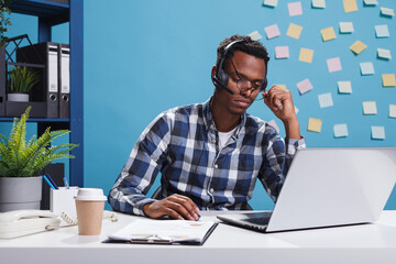 Wall Mural - stressed and fatigued telemarketer representative wearing headset while trying to help company clien