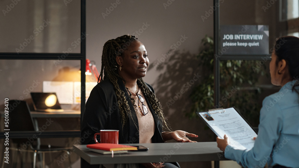 Young African woman presenting her resume to employer at table during ...