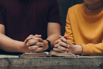 Wall Mural - young couples hands folded praying over a Bible. praying with his hands together over a closed Bible, Holy Bible in church concept for faith, spirituality, worship, and religion.