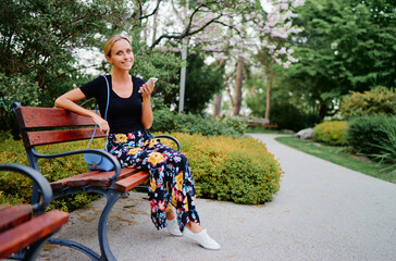 Wall Mural - Attractive young woman using smartphone while sitting at the city park.