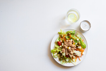  Tuna salad with lettuce, tomatos, carrot, corn  on white background with  glass water  and pepper pot,Flay lay with copy space