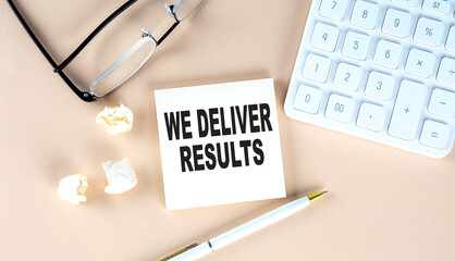 WE DELIVER RESULTS text on sticky with pen ,calculator and glasses on beige background