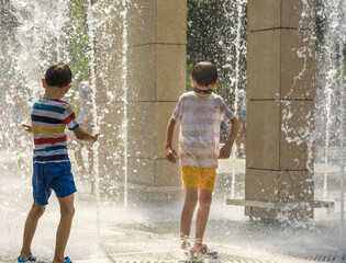 Wall Mural - Boy having fun in water fountains. Child playing with a city fountain on hot summer day. Happy kids having fun in fountain. Summer weather. Active leisure, lifestyle and vacation