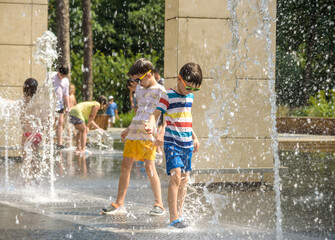 Wall Mural - Boy having fun in water fountains. Child playing with a city fountain on hot summer day. Happy kids having fun in fountain. Summer weather. Active leisure, lifestyle and vacation