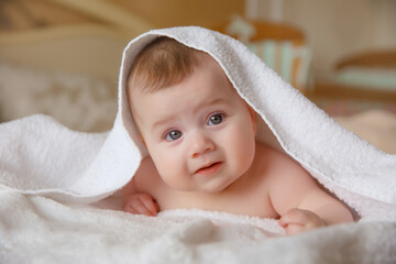 baby girl in a white towel or blanket in a white bedroom. a newborn baby is resting in bed. portrait