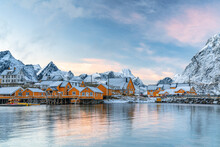 Fishermen's Wood Cabins Covered With Snow At Sunset In The Tiny Village Of Sakrisoy, Reine, Nordland, Lofoten Islands