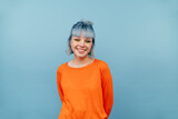 Fototapeta Uliczki - Smiling hipster girl with colored hair stands on a blue background with a happy face and looks at the camera.