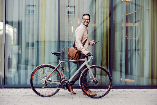 An urban man pushing bicycle and using phone while passing by window.