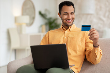 Smiling man using pc and credit card at home