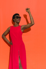Wall Mural - Confident black woman in elegant long red dress holding fist raised.