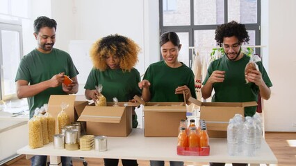 Wall Mural - charity, donation and volunteering concept - international group of happy smiling volunteers packing food in boxes at distribution or refugee assistance center