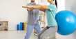 Young female patient together with physiotherapist does exercises for back with help of fitball. Cropped image woman perform squats with fitball to get rid of back pain and restore spine health.