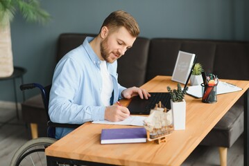 Wall Mural - Disabled person in the wheelchair works in the office at the computer. He is smiling and passionate about the workflow.