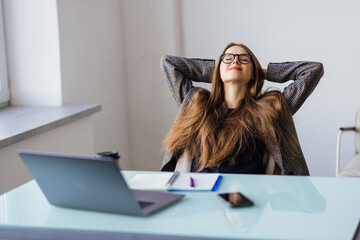 Calm smiling businesswoman relaxing at comfortable office chair hands behind head, happy woman resting in office satisfied after work done, enjoying break with eyes closed, peace of mind, no stress